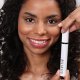 A woman confidently displays a tube of mascara