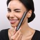 A woman smiles brightly while holding a mascara brush