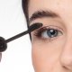 A woman applies mascara with a brush