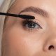 A woman carefully applies mascara to her eyelashes using a mascara brush