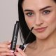 A woman grips a mascara tube and brush