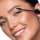 Model holding the mascara next to her left eye